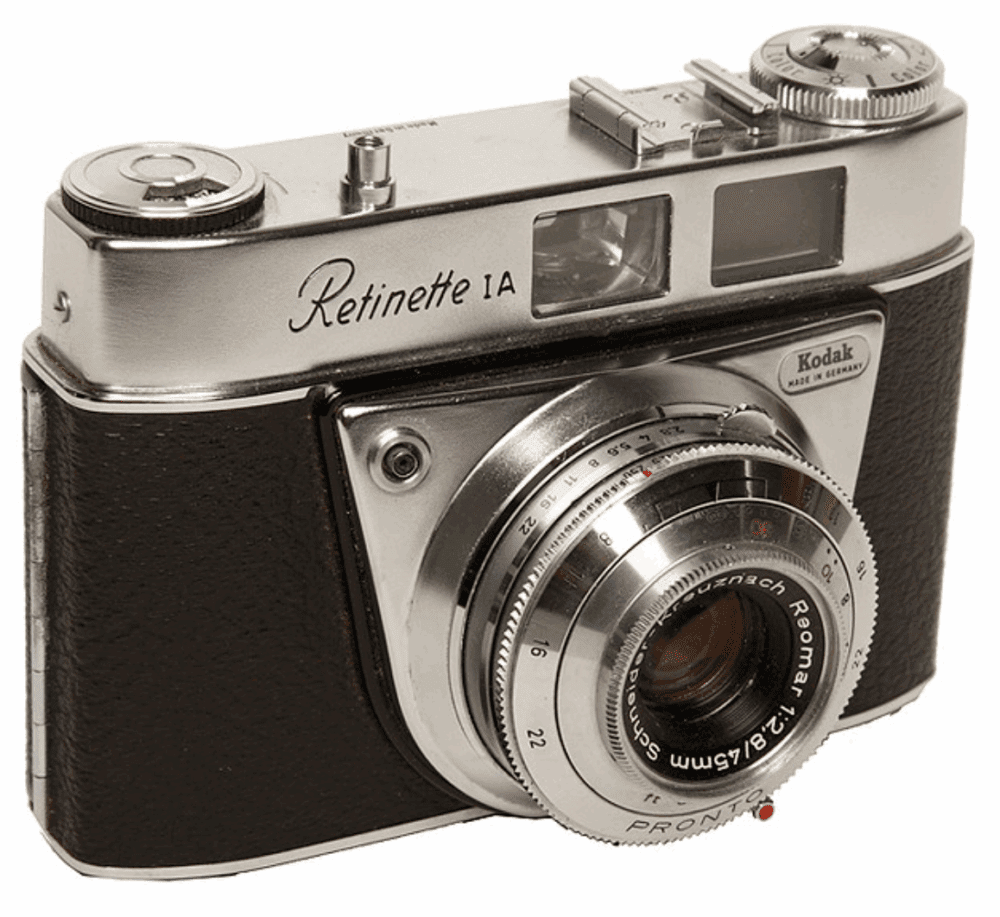 A vintage Kodak Retinette IA camera featuring a silver body with black textured detailing, a prominent lens labeled "Reomar f:2.8/45mm," and various dials and controls on the top.